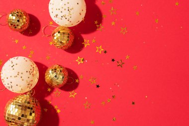 Noel kompozisyonu. Düz yerde, üst tarafta. Disko topu takısı, yıldız pırıltısı. Asgari yeni yıl partisi konsepti. Kırmızı arkaplanda fotokopi alanı olan beyaz ve altın Noel süslemeleri.