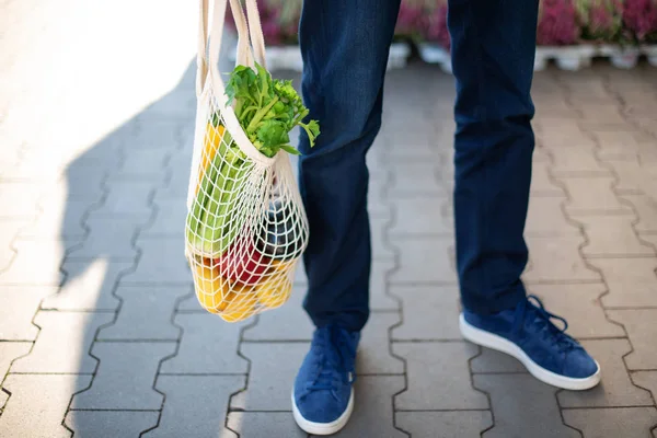 Zero waste concept with copy space. Young man holding cotton shopping bag with vegetables, products. Eco friendly mesh shopper. Zero waste, plastic free concept.