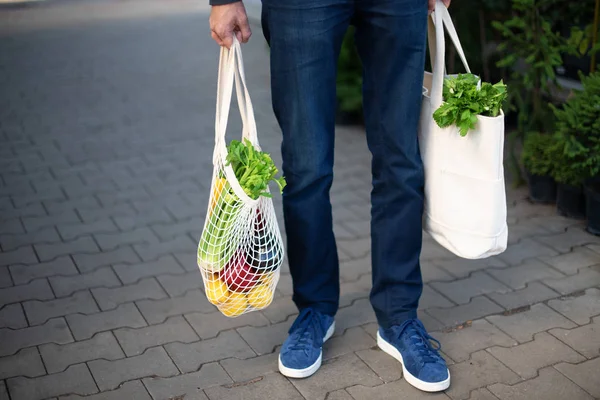 El hombre está sosteniendo la bolsa de compras de malla con engendros sin bolsas de plástico en el mercado de agricultores. Cero residuos, concepto libre de plástico. Estilo de vida sostenible — Foto de Stock