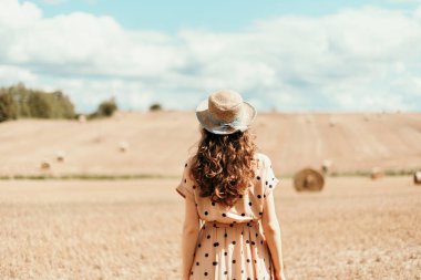 Hasat edilen tarlada saman balyalarıyla dikilen genç bir kadın. Fotokopi alanı olan tarım arka planı. Yaz ve sonbahar hasat konsepti. Şükran Günü