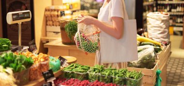 Kadın pazarda meyve ve sebze seçiyor. Sıfır atık, plastiksiz konsept. Sürdürülebilir yaşam tarzı. Alışveriş için tekrar kullanılabilir pamuk ve ağ eko torbaları.