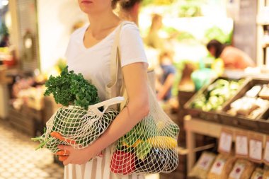 Naylon poşetsiz, ahşap arka planda sebzeli pamuk alışverişi yapan kız. Sıfır atık, plastiksiz konsept. Sürdürülebilir yaşam tarzı. Pankart.