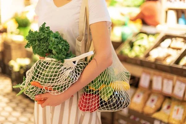 Zero waste concept with copy space. Woman holding cotton shopper and reusable mesh shopping bags with vegetables, products. Eco friendly mesh shopper. Zero waste, plastic free concept.