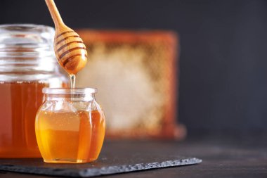 Bal kavanozu, bal peteği ve siyah arka planda bir kavanozda tahta kaşık. Uzayı kopyala Sonbahar hasat konsepti.