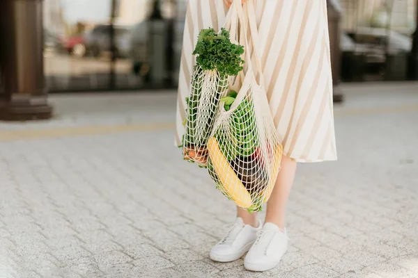 Chica sosteniendo bolsa de compras de malla y comprador de algodón con verduras sin bolsas de plástico, fondo de madera. Cero residuos, concepto libre de plástico. Estilo de vida sostenible. Banner. —  Fotos de Stock