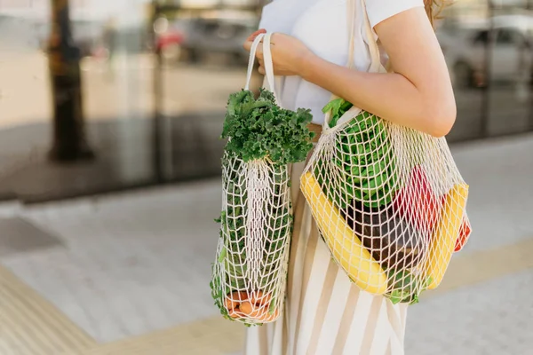 Chica sosteniendo bolsa de compras de malla y comprador de algodón con verduras sin bolsas de plástico, fondo de madera. Cero residuos, concepto libre de plástico. Estilo de vida sostenible. Banner. — Foto de Stock