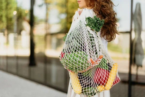 Zero waste concept with copy space. Woman holding cotton shopper and reusable mesh shopping bags with vegetables, products. Eco friendly mesh shopper. Zero waste, plastic free concept.