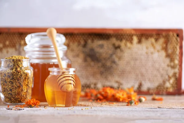 Kräuterhonig im Glas mit Dipper, Bienenwaben, Bienenpollengranulat, Ringelblumen auf grauem Hintergrund. — Stockfoto