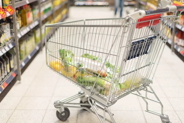 Grocery shopping cart full with food at blurred supermarket background. Copy space. Sustainable lifestyle. Sale, discount concept — Stock Photo, Image
