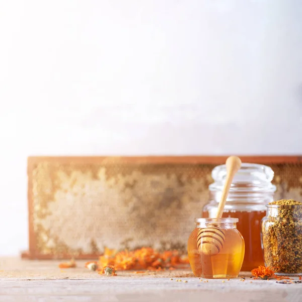 Φυτικό μέλι σε βάζο με σταγονόμετρο, κηρήθρα, κόκκους γύρης μέλισσας, άνθη καλέντουλας σε γκρι φόντο. — Φωτογραφία Αρχείου