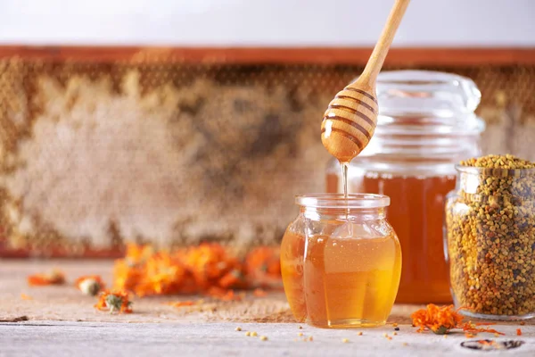 Kräuterhonig im Glas mit Dipper, Bienenwaben, Bienenpollengranulat, Ringelblumen auf grauem Hintergrund. — Stockfoto