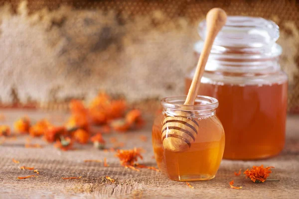 Kräuterhonig im Glas mit Dipper, Bienenwaben, Bienenpollengranulat, Ringelblumen auf grauem Hintergrund. — Stockfoto