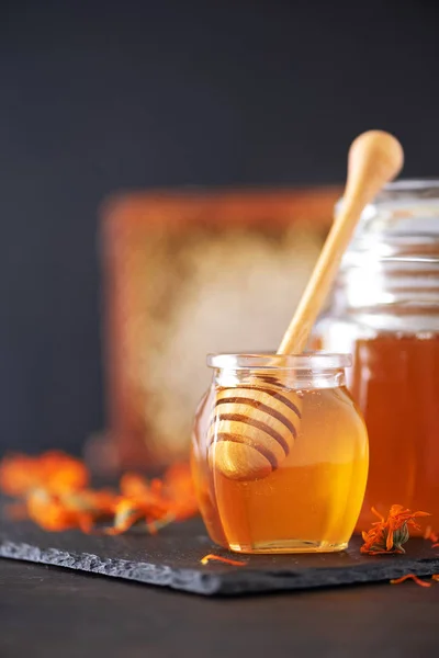 Herbal honey in jar with dipper, honeycomb, bee pollen granules, calendula flowers on black background. — 스톡 사진