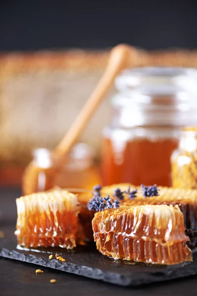 Včelí pylová zrnka, medová nádoba s dřevěným kapátkem, voštinové plástve na tmavém pozadí. Rozumím. Koncept podzimní sklizně — Stock fotografie