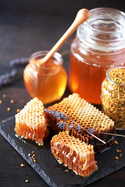 Honeycomb a medová nádoba s máčením na černém břidlicovém podnosu na tmavém pozadí. Rozumím. Horní pohled. — Stock fotografie