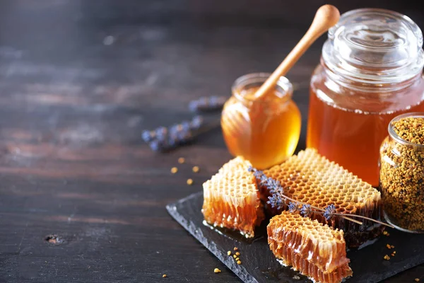 Včelí pylová zrnka, medová nádoba s dřevěným kapátkem, voštinové plástve na tmavém pozadí. Rozumím. Koncept podzimní sklizně — Stock fotografie