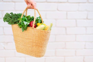 Sağlıklı organik sebzelerle dolu saman sepeti tutan bir kız, tuğla arka plan, fotokopi alanı. Sonbahar hasadı. Sıfır atık, plastiksiz konsept. Sürdürülebilir yaşam tarzı. Şükran Günü