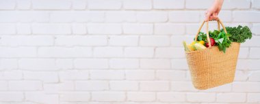 Tuğla kaplamalı organik sebzeli saman sepetini tutan kadın. Sağlıklı yiyecekler, vejetaryen diyeti. Çevre dostu, sıfır atık, plastik içermeyen konsept.