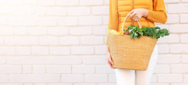 Tuğla kaplamalı organik sebzeli saman sepetini tutan kadın. Sağlıklı yiyecekler, vejetaryen diyeti. Çevre dostu, sıfır atık, plastik içermeyen konsept.