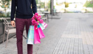 Pembe çiçekli romantik bir adam ve tuğla arka planda alışveriş torbaları. Kadınlar günü. Sevgililer Günü. Doğum günü partisi ya da romantik bir randevu için hazırım. Uzayı kopyala Bir deste kağıt hediye çantası.