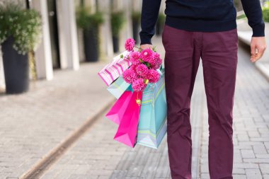 Pembe çiçekli romantik bir adam ve tuğla arka planda alışveriş torbaları. Kadınlar günü. Sevgililer Günü. Doğum günü partisi ya da romantik bir randevu için hazırım. Uzayı kopyala Bir deste kağıt hediye çantası.