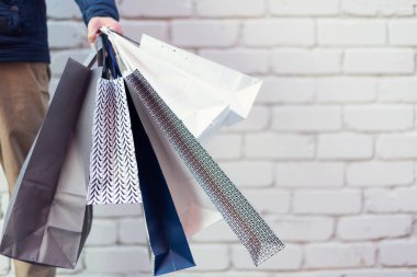Erkek el ele tutuşan bir grup alışveriş torbası ve tuğla arka planda alışverişler. Uzayı kopyala İndirim, indirim, Kara Cuma konsepti. Alışveriş merkezi ve priz