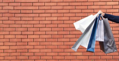 Erkek el ele tutuşan bir grup alışveriş torbası ve tuğla arka planda alışverişler. Uzayı kopyala İndirim, indirim, Kara Cuma konsepti. Alışveriş merkezi ve priz