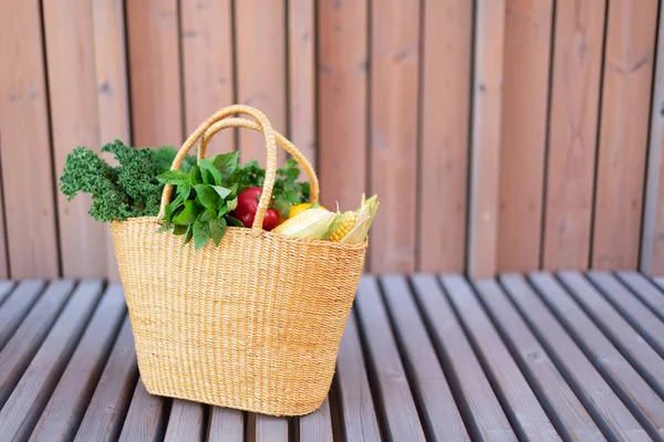 Cesta de paja de mano de mujer con verduras orgánicas sobre fondo de madera. Comida saludable, dieta vegetariana. Ecológico, cero residuos, concepto libre de plástico . — Foto de Stock