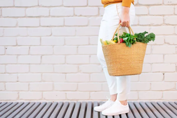 Niña sosteniendo cesta de paja con verduras, productos sin bolsas de plástico, fondo de ladrillo. Cero residuos, concepto libre de plástico. Estilo de vida sostenible. Banner . — Foto de Stock