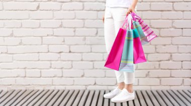 Tuğla arka planda çiçek ve alışveriş torbaları tutan kadın eller. Kadınlar günü. Sevgililer Günü. Doğum günü partisine hazırım. Uzayı kopyala Bir deste kağıt hediye çantası.