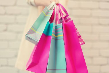 Tuğla arka planda çiçek ve alışveriş torbaları tutan kadın eller. Kadınlar günü. Sevgililer Günü. Doğum günü partisine hazırım. Uzayı kopyala Bir deste kağıt hediye çantası.