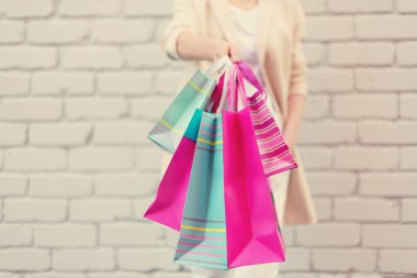 Tuğla arka planda çiçek ve alışveriş torbaları tutan kadın eller. Kadınlar günü. Sevgililer Günü. Doğum günü partisine hazırım. Uzayı kopyala Bir deste kağıt hediye çantası.