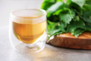 Isırgan otlu bir fincan sağlıklı bitki çayı. Alternatif bitkisel ilaç. Isırgan otu, urtica. Cilt alerjisi bakımı. Gri arka planda taze ısırgan otları