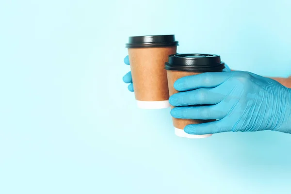 Coffee cup in hand with medical glove on blue background. Banner with copy space. Contactless delivery service during quarantine coronavirus pandemic. Take away only concept. Delivery service concept.