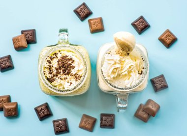 mason kavanoz krem üst ile iki muz ve kivi milkshakes çikolata parçaları ile dekore edilmiştir. mavi moda arka plan üzerinde düz yatıyordu üstten görünüm güler yüzlü. çikolata ve milkshake ile yaratıcı düzeni