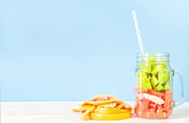 mavi ve beyaz tahta üzerinde içme bir saman ve greyfurt kabuğu bir mason kavanoza taze meyve kesme