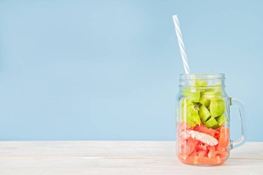 içme pipet mavi ve beyaz tahta üzerinde bir mason kavanoza taze meyve kesme