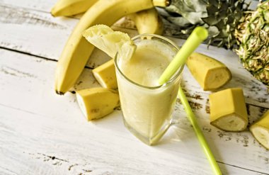 Muz ve ananas ananas kokteyli veya beyaz tahta masada saman suyu cam bir içme ile dekore edilmiş