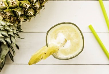 Üstten görünüm yatıyordu ananas kokteyli veya beyaz tahta masada muz ve ananas düz ile dekore edilmiş içme bir saman ile cam suyu