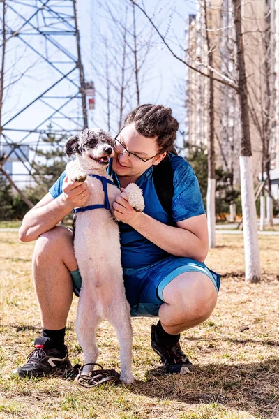 Happy young man holding dog outdoors in the urban park in a sunny day