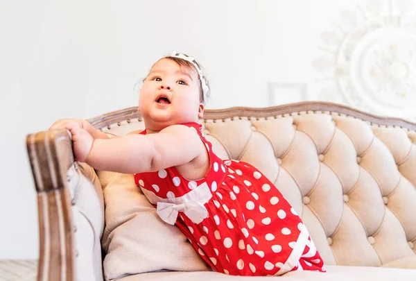 Lovely asian baby in a red dress playing on the sofa indoors