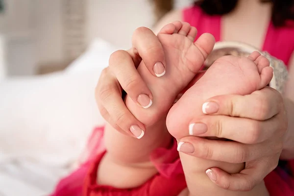Mãe mãos segurando pés de bebê na cama branca — Fotografia de Stock
