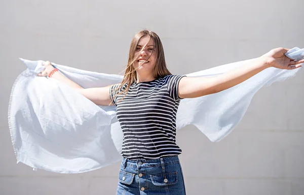 Happy young caucasian woman with light blue fabric having fun and laughing outdoors in a sunny day in summer