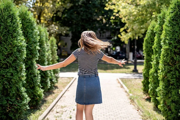 公園の木々の背景を振り返る楽しみを持っているカジュアルな服を着た若いかわいい白人女性 — ストック写真