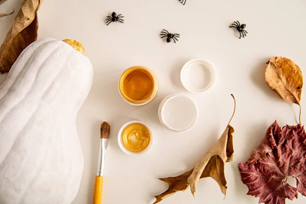 Hermosa calabaza de halloween pintada de blanco y oro sobre mesa blanca decorada con arañas y hojas de otoño — Foto de Stock