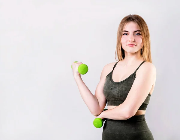 Ung fit kvinde holder håndvægte isoleret på grå baggrund - Stock-foto