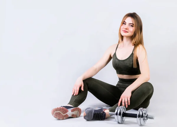 Ung fit kvinde sidder med håndvægte isoleret på grå baggrund - Stock-foto