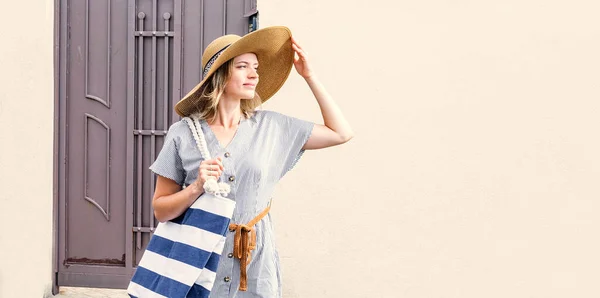 Ung blond kaukasisk kvinna i sommarkläder och hatt står utomhus på gatan och tittar mot solen — Stockfoto