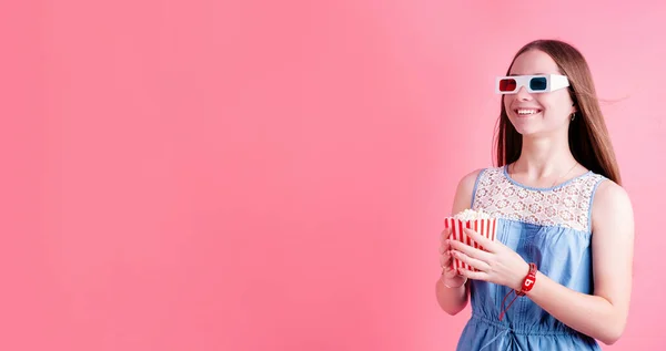 興奮したティーンエイジャーの女の子は 映画を見て コピースペースでピンクの背景に隔離されたポップコーンを食べて3Dメガネをかけています バナー — ストック写真