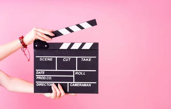 A movie production clapper board. Female hands holding a clapper board isolated on pink